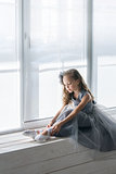 Little ballerina in gray dress puts on ballet shoes pointe front
