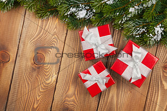 Christmas fir tree with snow and red gift boxes on rustic wooden