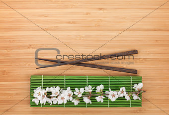 Chopsticks and sakura branch over bamboo mat