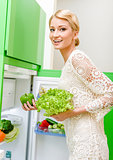 Smiling young woman taking vegetables out of fridge
