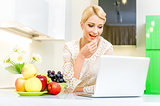 Beautiful young woman using her laptop computer in the kitchen