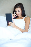 Beautiful young girl reading a tablet in bed