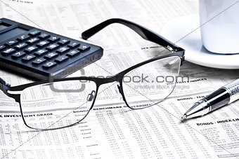 detail of a pen and glasses near a calculator with cup of coffee 