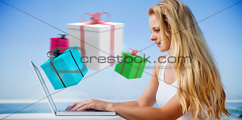 Composite image of pretty blonde using her laptop at the beach