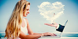 Composite image of pretty blonde using her laptop at the beach