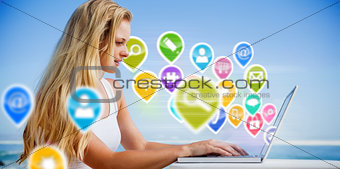 Composite image of pretty blonde using her laptop at the beach