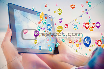 Composite image of woman sitting on beach in deck chair using tablet pc