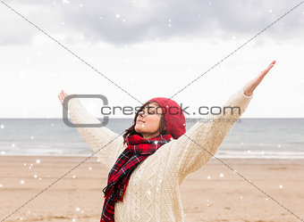 Composite image of woman in warm clothing stretching arms at beach