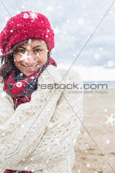 Composite image of cute smiling woman in stylish warm clothing on the beach