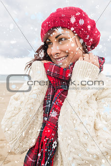 Composite image of cute smiling woman in warm clothing looking away at beach