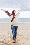 Composite image of woman in warm clothing stretching her arms at beach