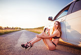 Attractive young woman sitting at car and drinking water