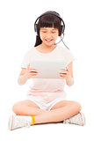 sitting little girl holding a tablet with earphone.