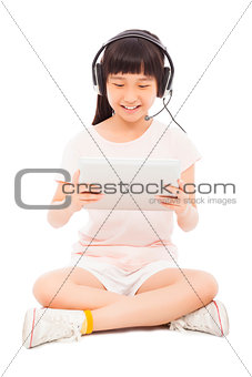sitting little girl holding a tablet with earphone.