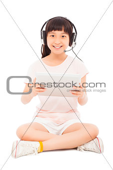 smiling little girl stiiting and holding a tablet with earphone