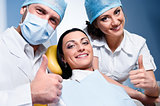 Friendly male dentist with assistant and smiling patient showing thumb up