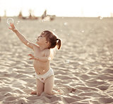 Adorable baby girl playing with soap bubbles on the beach