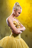Sad ballerina in yellow tutu posing over obsolete wall
