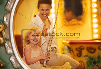 Portrait of happy mother and baby girl riding on carousel