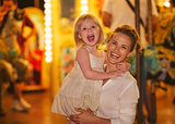 Portrait of smiling mother and baby girl in front of carousel