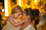 Portrait of mother and baby girl hugging in front of carousel