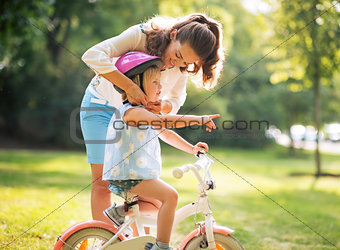 Mother wearing helmet on baby girl on bicycle