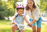 Happy mother helping baby girl riding on bicycle