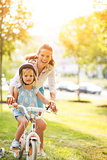 Portrait of happy mother helping baby girl riding bicycle in par
