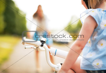 Closeup on baby girl sitting on bicycle and mother waiting in ba