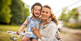 Portrait of smiling mother and baby girl sitting on bicycle