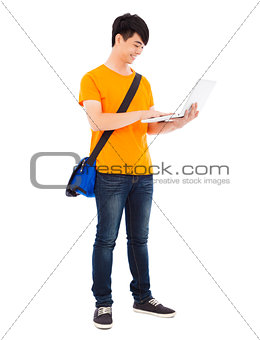 Smiling young student standing and using laptop