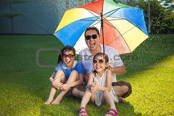 Father and two daughters sitting on a meadow with colorful umbre