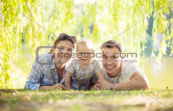 Happy parents with toddler boy. Mother, father and son relaxing on the lawn.