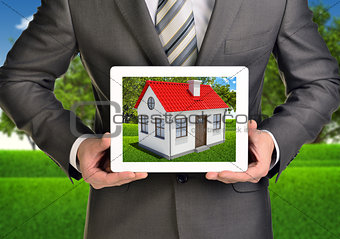 Hands hold tablet pc. Picture of small house with red roof on screen