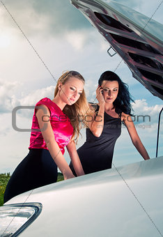 Two young women with broken car on a road