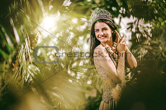 Elegant smiling lady with tiara on a head posing in a forest