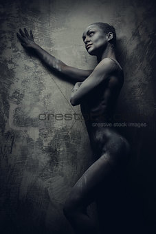Naked sportive woman painted in grey color posing over grey wall