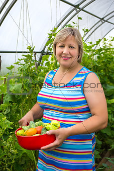 Portrait of a middle-aged woman with vegetables in a bowl near greenhouses
