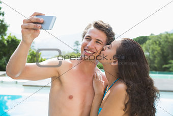 Couple taking picture of themselves by swimming pool on a sunny day