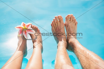 Couple feet against swimming pool on a sunny day