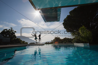Cheerful young couple jumping into swimming pool