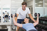 Personal trainer helping client lift dumbbells
