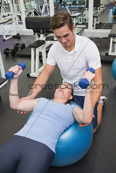 Personal trainer helping client lift dumbbells
