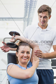 Personal trainer helping client lift dumbbell