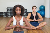 Fit couple sitting in lotus pose in fitness studio
