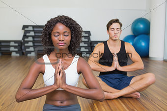 Fit couple sitting in lotus pose in fitness studio