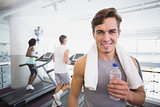 Fit man smiling at camera beside treadmills