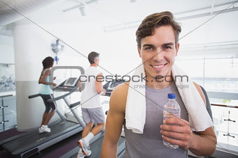 Fit man smiling at camera beside treadmills