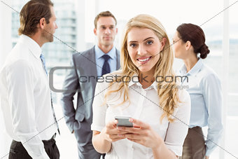 Businesswoman text messaging with colleagues in meeting behind
