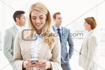 Businesswoman text messaging with colleagues in meeting behind